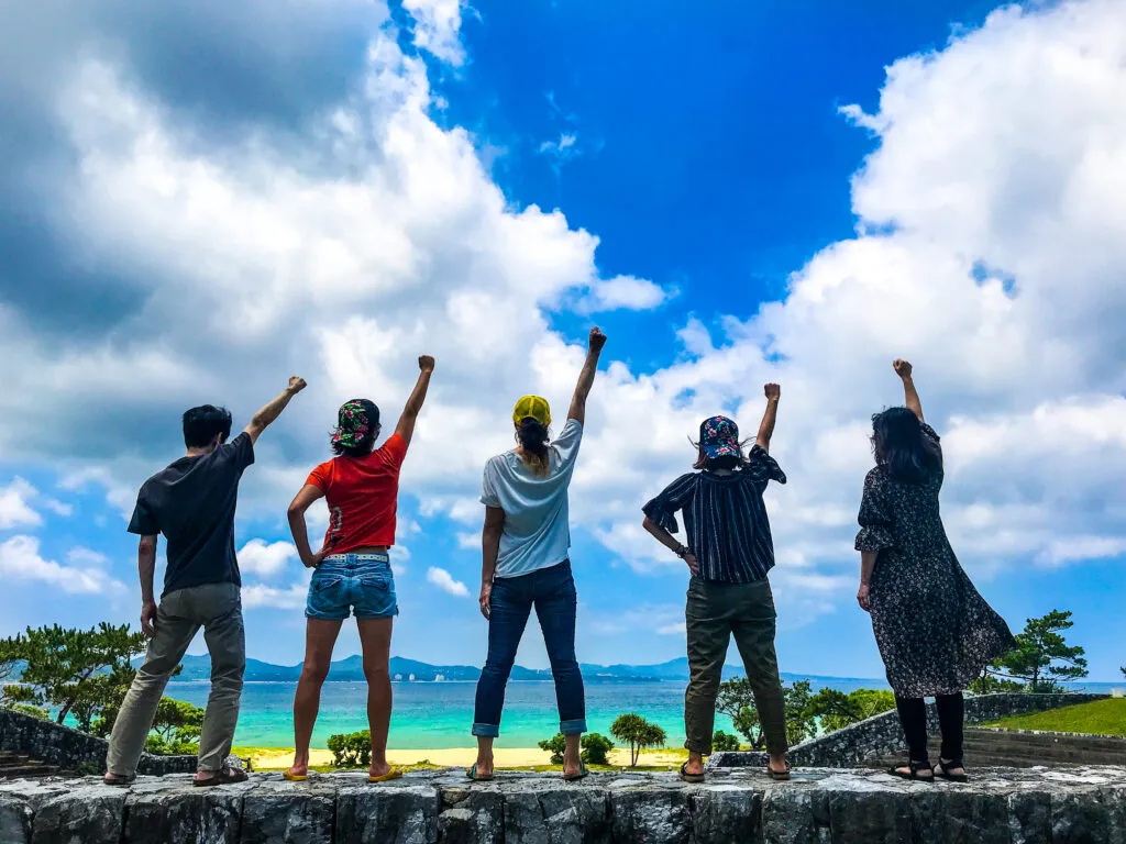 沖縄の海辺で右腕を挙げる仲間たち