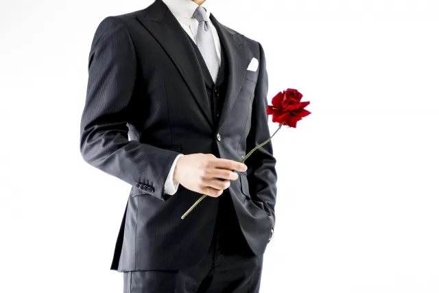 右手でバラをもつスーツの男性